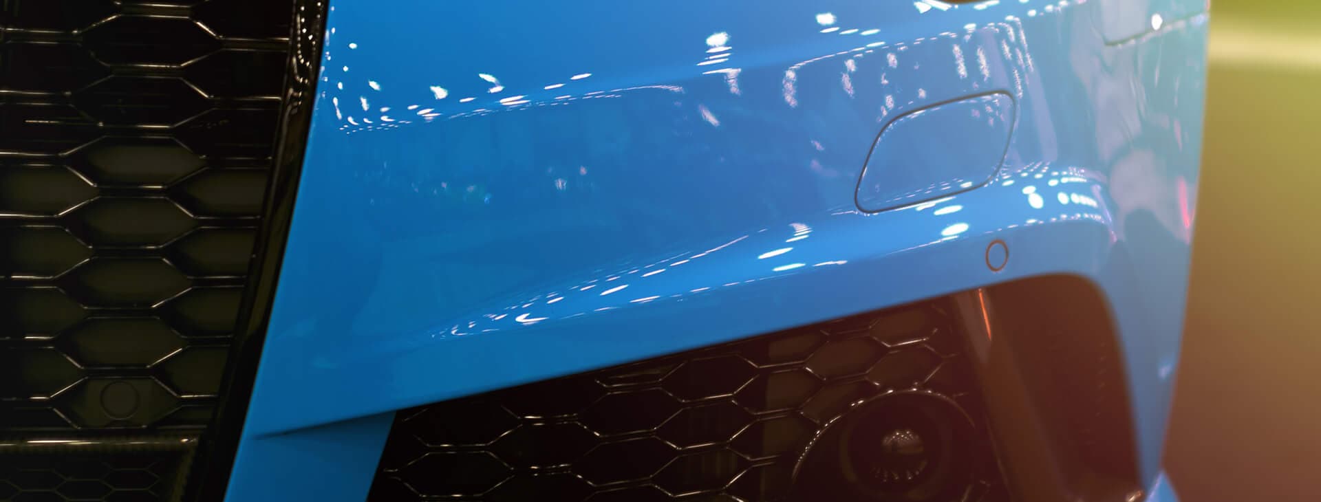 front bumper of a blue sports car with a black headlight and spoiler for automotive markets and applications